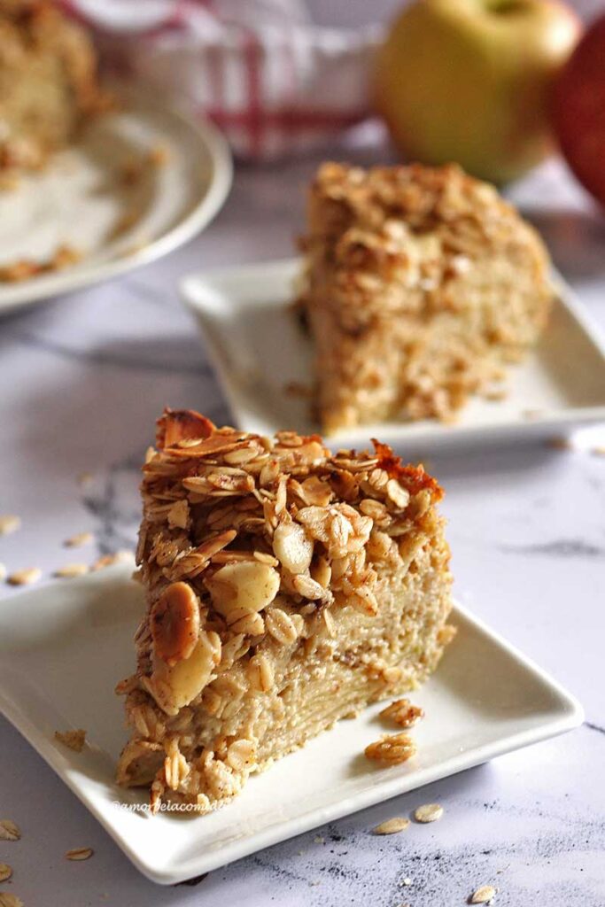 Duas fatias de torta de maçã, cada uma em um prato quadrado pequeno, no topo da torta uma camada crocante de flocos de aveia e amêndoas laminadas