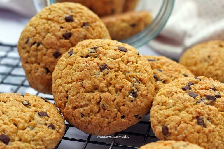 RECEITA DE BROA DE FUBÁ SIMPLES COM AVEIA Várias broas de fubá redondas com pedacinhos de chocolate sobre grade, ao fundo o vidro deitado com mais broas dentro