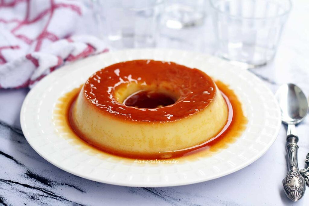 Pudim redondo com furo no meio, cobertura caramelizada, ao redor do pudim mais calda de caramelo