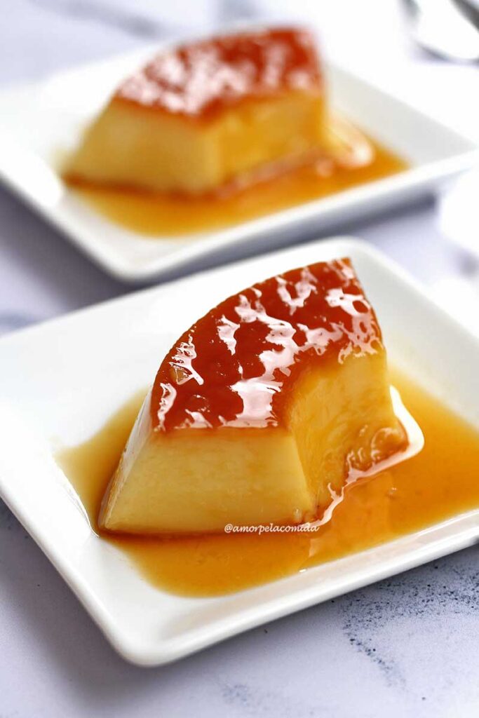 Duas fatias de pudim, cada uma em um prato quadrado pequeno, o topo é caramelizado e ao redor da fatia tem calda de caramelo