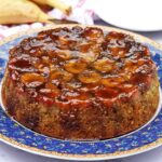 Bolo com o topo coberto de bananas caramelizadas, ao fundo algumas bananas e pratos redondos pequenos