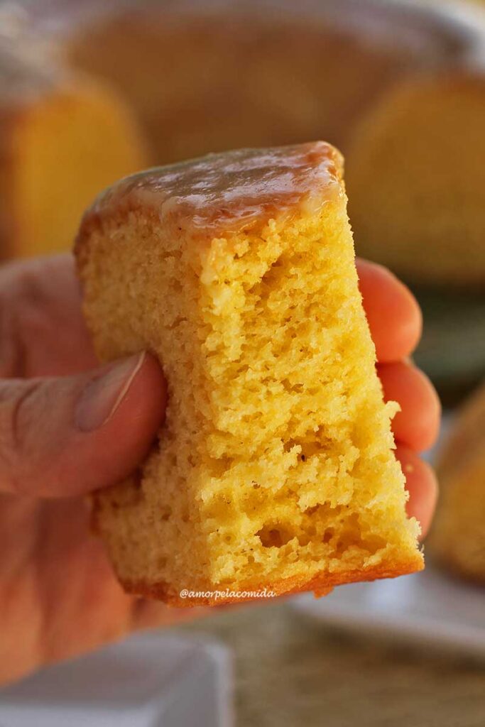 Mão segurando pedaço de bolo de fubá já mordido, mostrando a textura aerada e leve do bolo