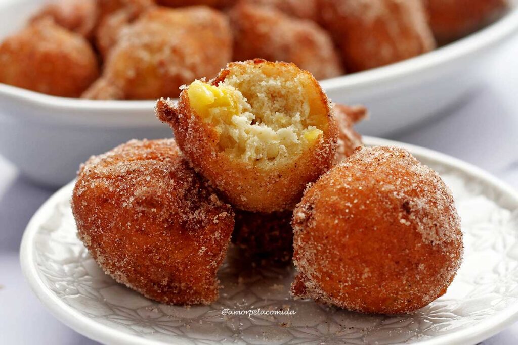 Três bolinho de chuva em um prato redondo pequeno, o que está por cima, está mordido