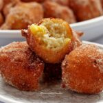 Três bolinho de chuva em um prato redondo pequeno, o que está por cima, está mordido