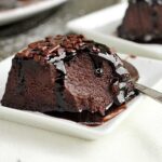 fatia de pudim de chocolate com calda de chocolate e cobertura de granulado de chocolate já faltando uma colherada da fatia