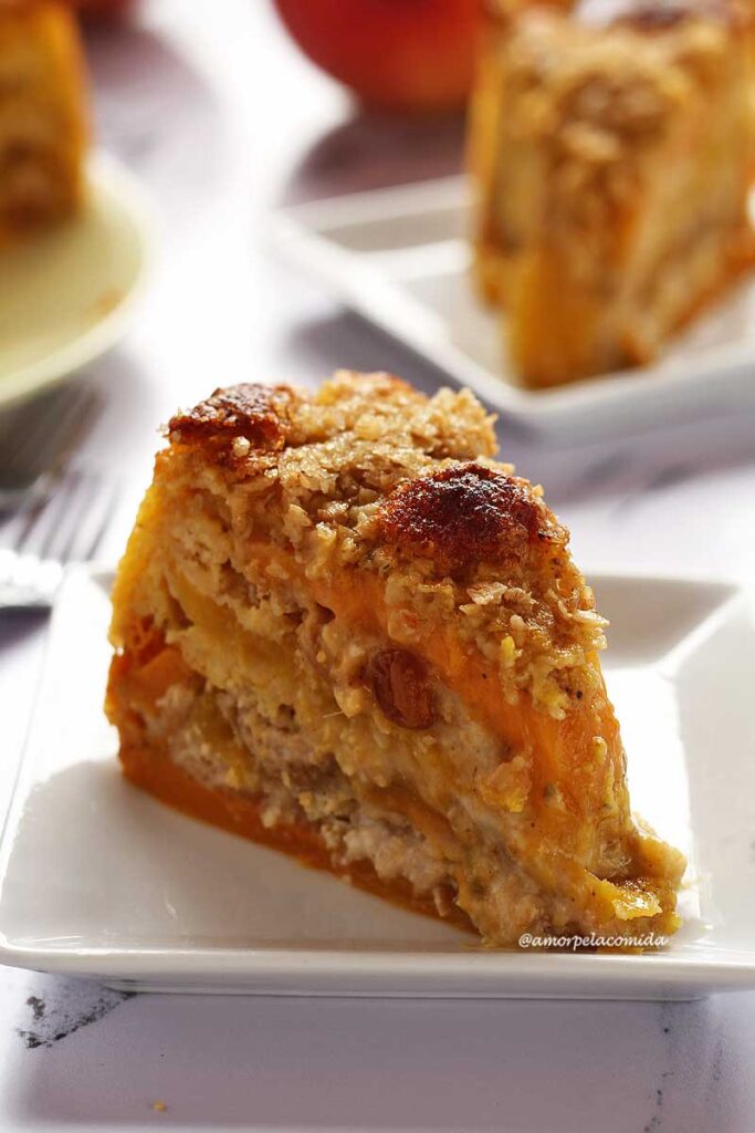 Fatia de torta de manga sobre prato quadrado pequeno, ao fundo mais um pedaço desfocado