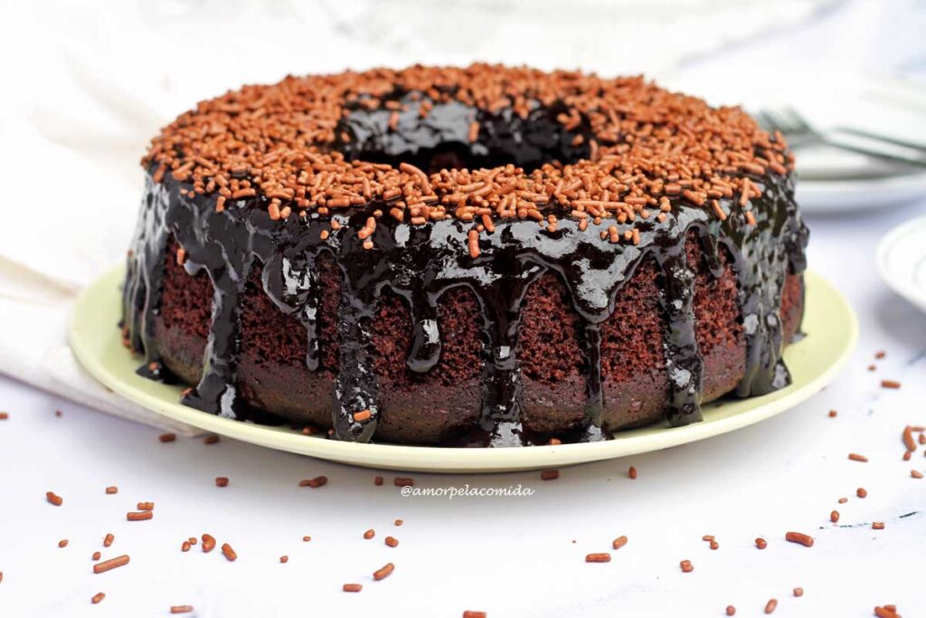Bolo redondo com furo no meio de chocolate com cobertura de chocolate escorrendo pelas laterais e granulado por cima