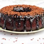 Bolo redondo com furo no meio de chocolate com cobertura de chocolate escorrendo pelas laterais e granulado por cima