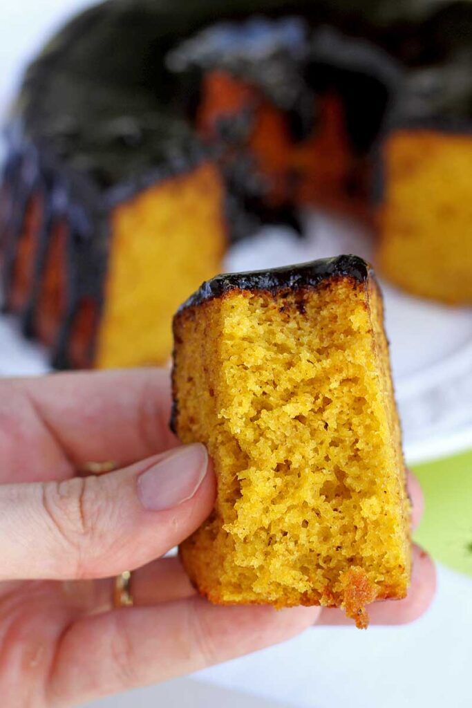 mão segurando fatia de bolo de cenoura mordido, mostrando a textura aerada e macia da massa