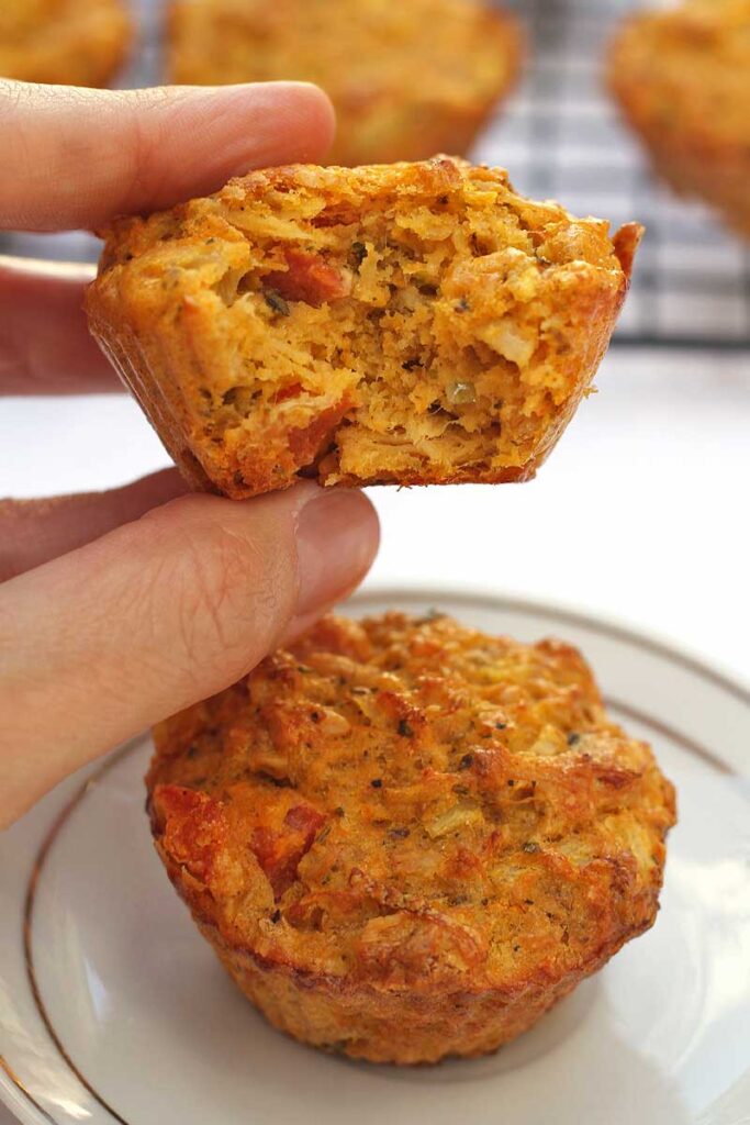 Mão segurando tortinha de frango mordida, abaixo mais uma tortinha sobre prato redondo pequeno