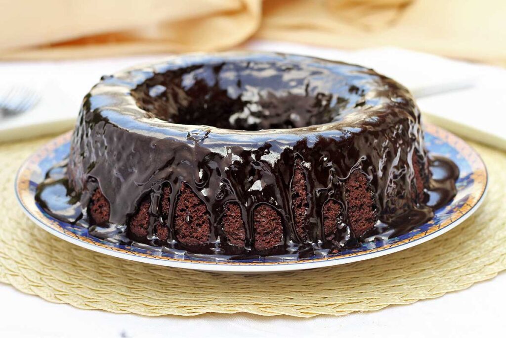 bolo redondo com furo no meio com cobertura de chocolate cremosa escorrendo por cima