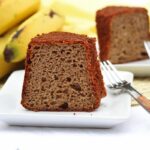Duas fatias sobre 2 pratos quadrados pequenos, ao fundo um cacho de banana, ao lado de cada prato, um garfinho
