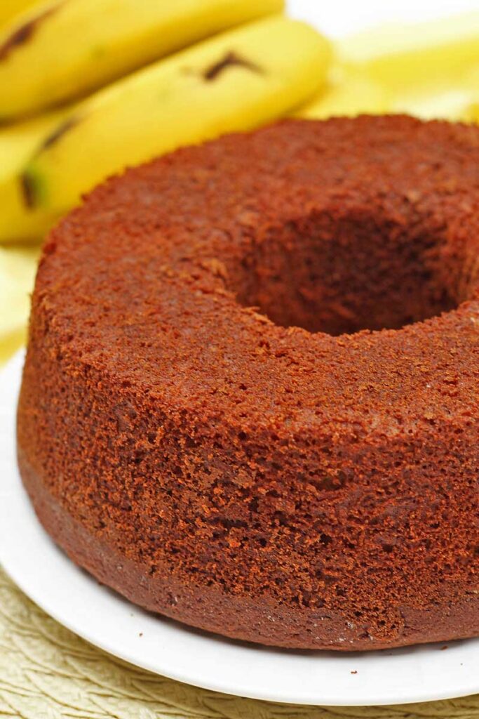 Bolo redondo com furo no meio, ao fundo aparece uma parte do cacho de banana
