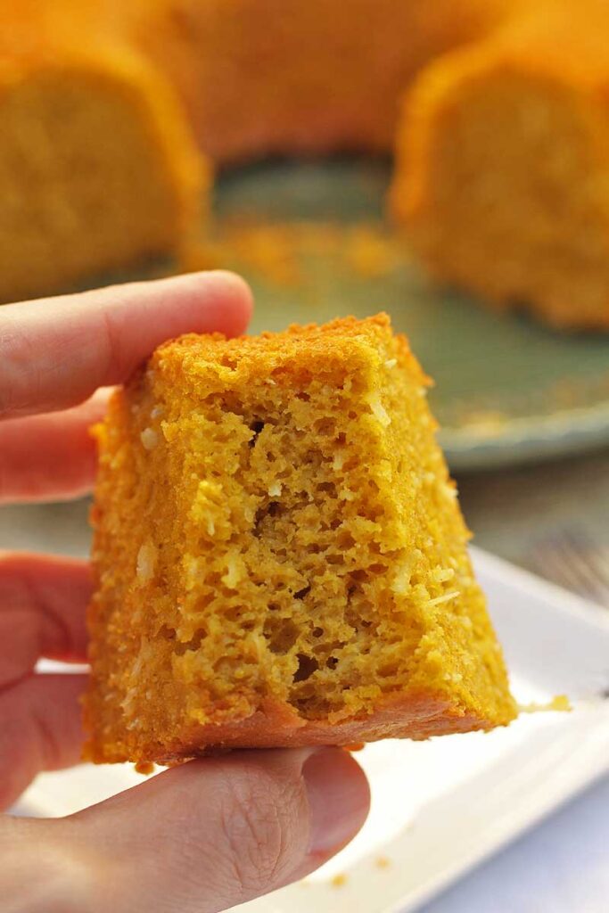 Mão segurando fatia de bolo de abóbora com coco mordida