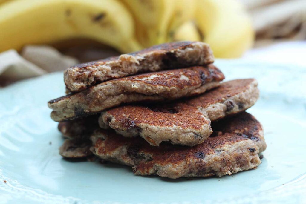 Uma pilha com 4 panquecas, a de cima já está mordida, ao fundo um cacho de banana