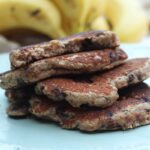 Uma pilha com 4 panquecas, a de cima já está mordida, ao fundo um cacho de banana