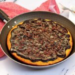Frigideira antiaderente com bolo de cenoura dentro, esse bolo tem cobertura de chocolate e granulado de chocolate por cima