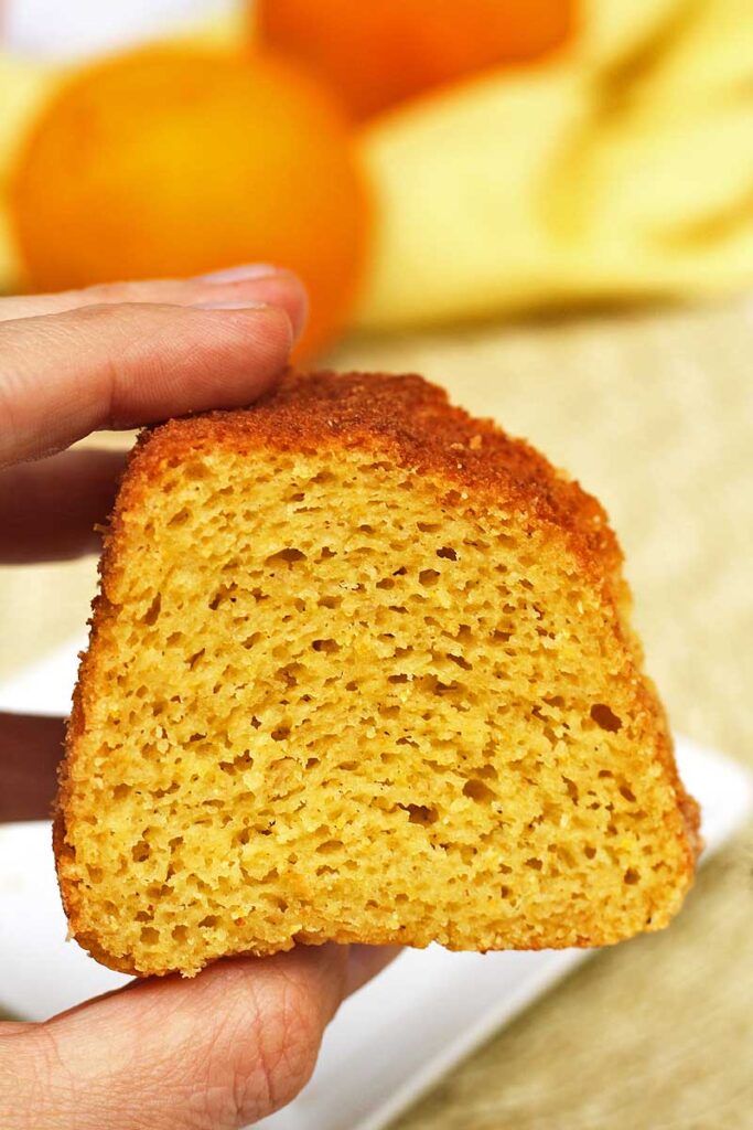 mão segurando fatia de bolo, ao fundo, laranjas desfocadas