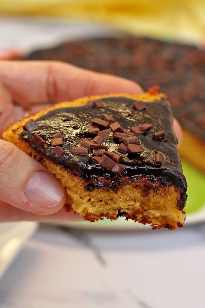 mão segurando fatia de bolo de cenoura com cobetrura de chocolate já mordido