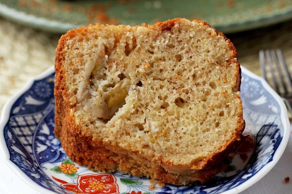 Fatia de bolo de banana e laranja deitada sobre um prato redondo pequeno com estampa oriental
