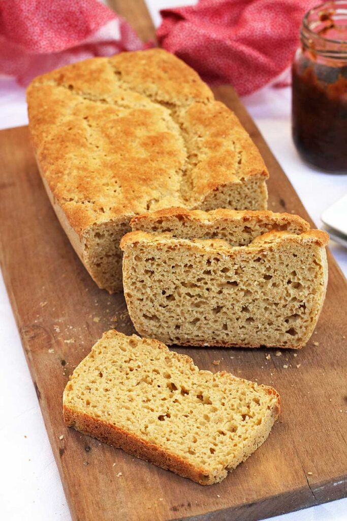 Pão com 3 fatias cortadas, duas apoiadas no pão, uma fatia apoiada na tábua de madeira