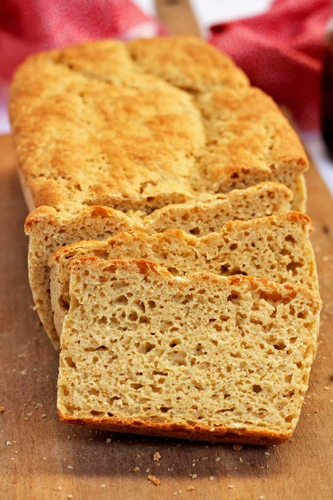 Pão caseiro fatiado, tem 3 fatias do pão apoiado no pão caseiro, sobre uma tábua de madeira