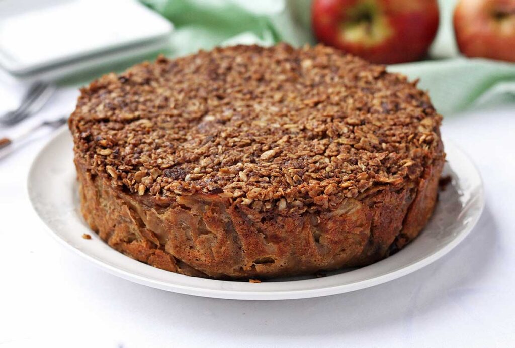 Torta redonda com cobertura de aveia misturada com açúcar mascavo, ao fundo pratos e maçãs