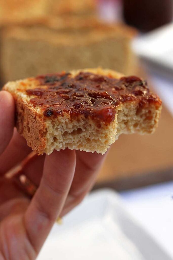 mão segurando fatia de pão com geleia, o pão já está mordido duas vezes