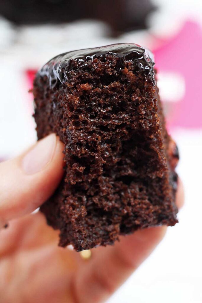 mão segurando fatia de bolo de café com cobertura cremosa, o bolo já foi mordido e é possível ver uma textura bem fofa e aerada da massa
