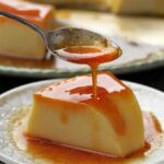 fatia de pudim dobre prato redondo pequeno, acima da fatia uma colher pequena derramando caramelo por cima