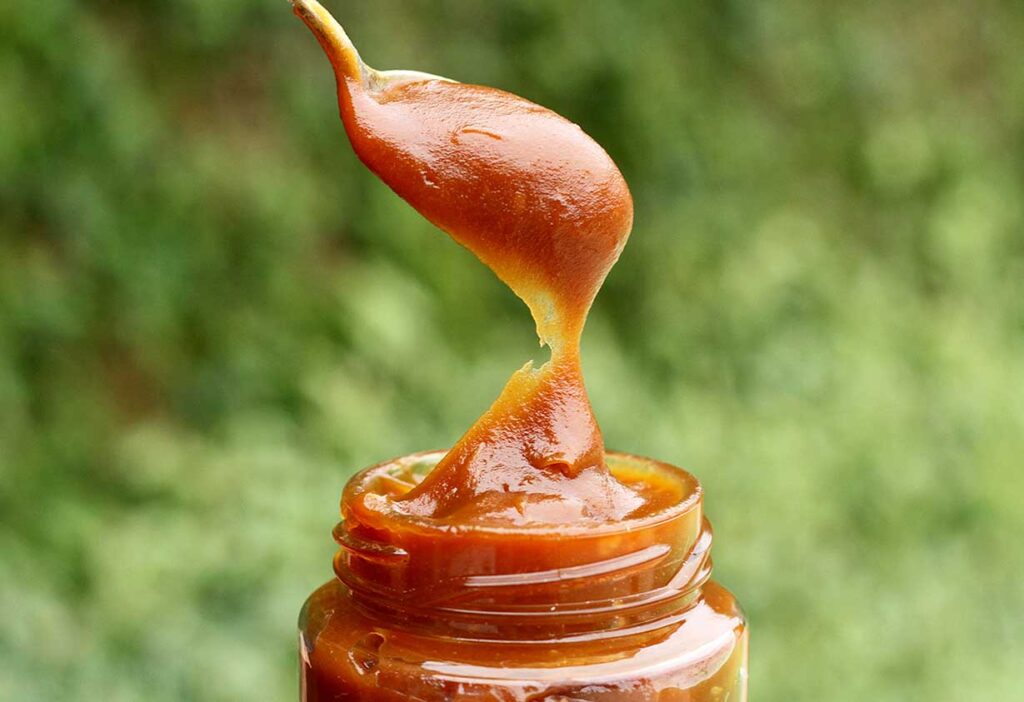 Vidro de doce de leite com colher cheia de doce de leite saindo de dentro do pote