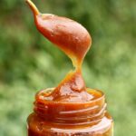 Vidro de doce de leite com colher cheia de doce de leite saindo de dentro do pote