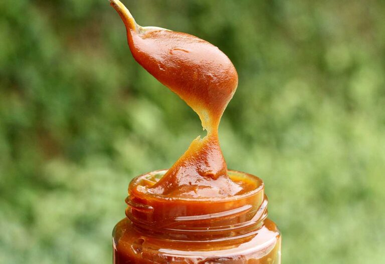 Vidro de doce de leite com colher cheia de doce de leite saindo de dentro do pote
