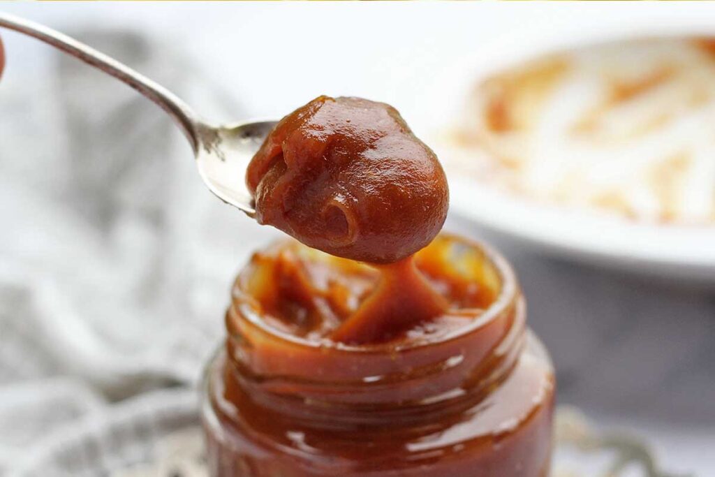 Vidro de doce de leite com colher cheia de doce de leite saindo de dentro do pote