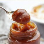 Vidro de doce de leite com colher cheia de doce de leite saindo de dentro do pote