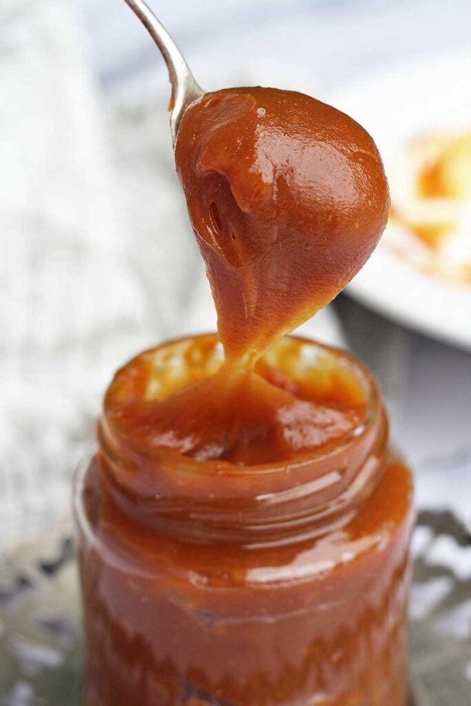 Vidro de doce de leite com colher cheia de doce de leite saindo de dentro do pote